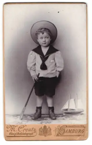 Fotografie M. Creutz, Hamburg, junger Knabe in Matrosenkleidung nebst Spielzeug Segelschiff
