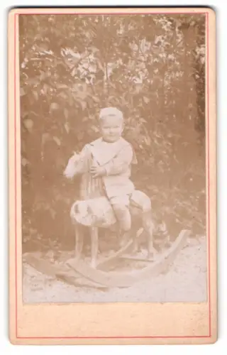 Fotografie niedlicher kleiner Junge auf seinem Schaukelpferd