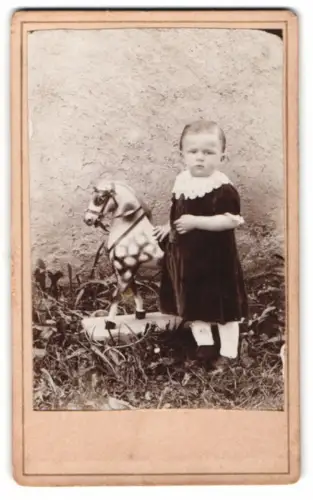 Fotografie kleines Mädchen im dunklen Kleid mit Spielzeug Pferd auf Rollen