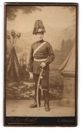Fotografie Fritz Kühl, Landau, Soldat in Uniform mit Pickelhaube Rosshaarbusch und Säbel vor einer Studiokulisse