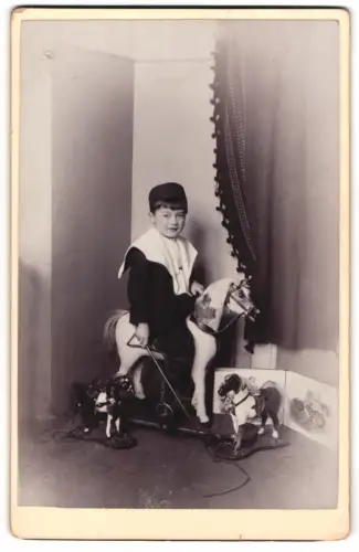 Fotografie junger Knabe mit Spielzeug Pferd auf Rollen und Reitgerte
