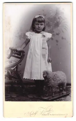 Fotografie Adolf Köster, Hagen i. W., junges Mädchen im weissen Kleid mit Stoffschaaf auf Rollen