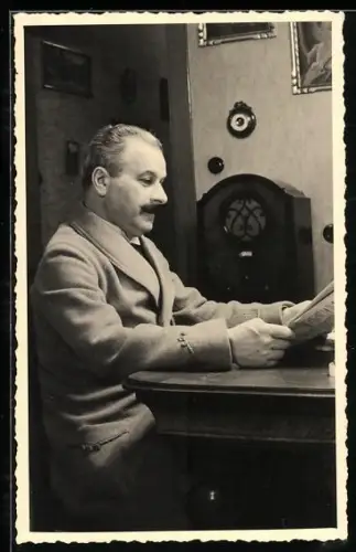 Foto-AK Mann sitzt mit einer Zeitung am Tisch und hört Radio