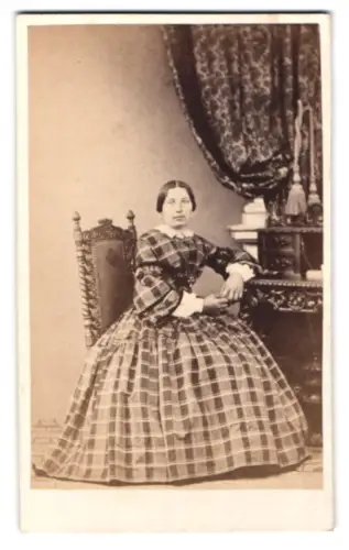 Fotografie unbekannter Fotograf und Ort, Frau in kariertem Kleid neben Tisch