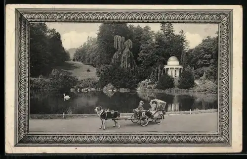 AK Hund zieht eine Mini-Kutsche mit Puppen, Parkpanorama mit Teich