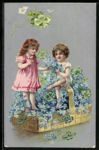 Präge-AK Zwei Kinder sitzen auf einem Korb voller Vergissmeinnicht und Klee