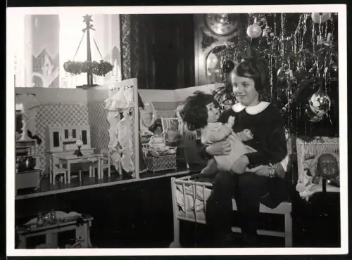 Fotografie kleines Mädchen zu Weihnachten mit Puppenhaus und grosser Puppe auf dem Schoss