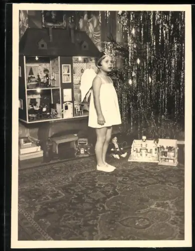 Fotografie kleines Mädchen als Weihnachtsengel vor einer Puppenstube und geschmückten Weihnachtsbaum