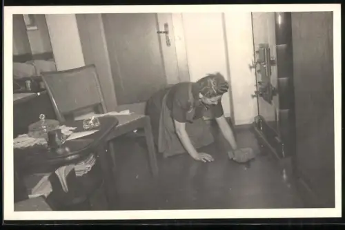 Fotografie Hausfrau beim Hausputz mit Kittel, wischt den Boden vor dem Kachelofen