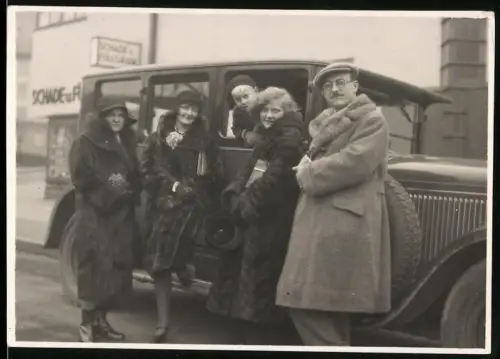 Fotografie junge Frauen und Mann in Pelzmänteln am Auto gelehnt
