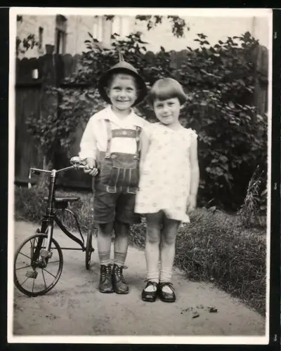 Fotografie Knabe in Tracht und Mädchen mit ihrem Dreirad