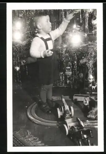 Fotografie junger Knabe schmückt den Weihnachtsbaum, Spielzeug am Boden