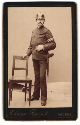 Fotografie Johann Fiausch, Voitsberg, Feuerwehrmann in Uniform mit Axt an der Seite und Helm
