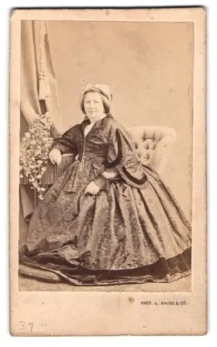 Fotografie L. Haase & Co., Berlin, Friedrichstrasse 178, Dame Charlotte Movins im eleganten Kleid auf Sessel