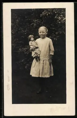 Foto-AK Blondes kleines Mädchen mit Puppe in einem Garten