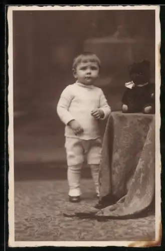 Foto-AK Kleines Kind neben Teddy auf einem Tisch