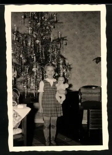 Fotografie kleines Mädchen an Weihnachten mit ihrer Puppe vor dem Weihnachtsbaum, 1953