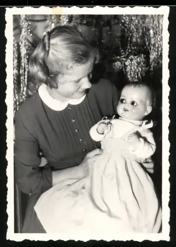 Fotografie junges Mädchen mit ihrer Puppe im Arm vor dem Weihnachtsbaum
