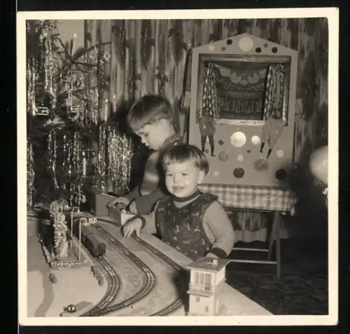Fotografie zwei Knaben Michi & Peterle spielen mit Modelleisenbahn, Kasperle Theater im Hintergrund