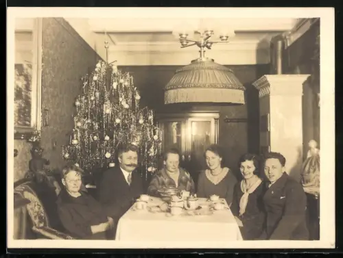 Fotografie Weihnachten, Familie am Kaffeetisch mit geschmücktem Weihnachtsbaum
