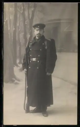 Foto-AK Soldat im Mantel mit Tornister, Signalpfeife, Schirmmütze und Gewehr