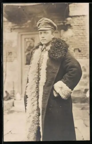 Foto-AK Soldat in Feldgrau-Uniform mit Pelzmantel und Schirmmütze