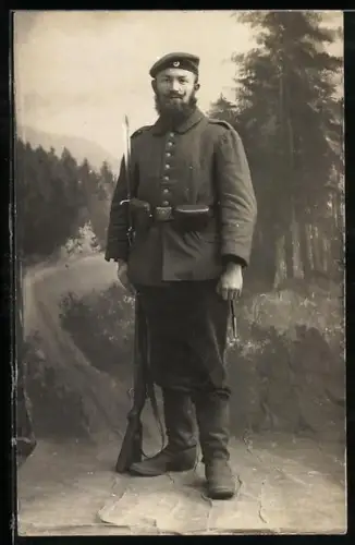 Foto-AK Soldat in Feldgrau Uniform mit Krätzchen, Koppeltaschen und Gewehr mit aufgepflanztem Bajonett