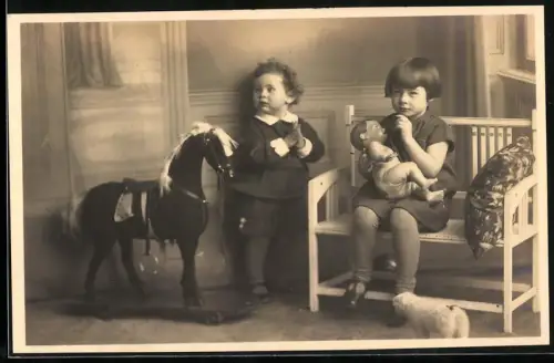 Fotografie zwei Kinder mit Schaukelpferd auf Rollen und Puppe im Arm