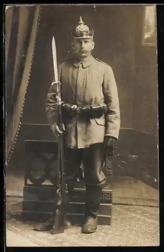 Foto-AK Bayerischer Soldat in Feldgrau Uniform mit Pickelhaube, Patronentaschen und Gewehr mit aufgepflanztem Bajonett
