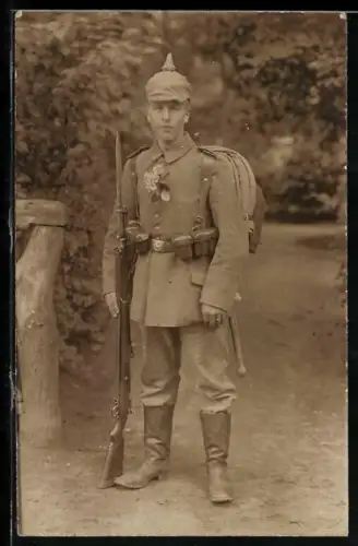 Foto-AK Soldat in Feldgrau Uniform mit Pickelhaube mit Überzug, Patronentaschen, Feldspaten und Gewehr