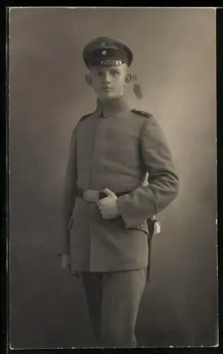 Foto-AK Soldat in Feldgrau Uniform mit verdeckter Knopfleiste, Schirmmütze und Bajonett
