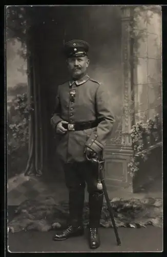 Foto-AK Feldwebel in Feldgrau Uniform mit Schirmmütze, Orden und Säbel