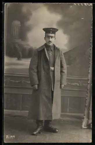 Foto-AK Soldat in Feldgrau Uniform mit Mantel, Schirmmütze und Band zum EK II 1914