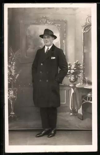 Foto-AK Mann im Mantel mit Hut vor einer Studiokulisse