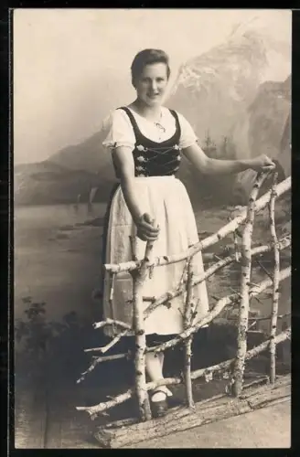 Foto-AK Dame in Tracht steht hinter einem rustikalen Zaun