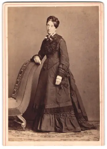 Fotografie unbekannter Fotograf und Ort, ältere Dame im dunklen Biedermeierkleid posiert am Sessel