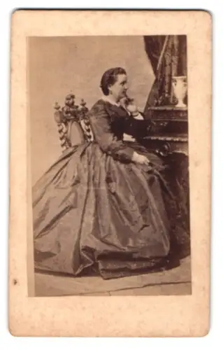 Fotografie C. S. Bomsdorf, Neubrandenburg, junge Dame im weiten Kleid sitzend am Sekretär