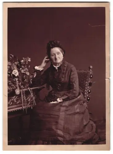 Fotografie unbekannter Fotograf und Ort, Sitzende Dame neben Blumenarrangement