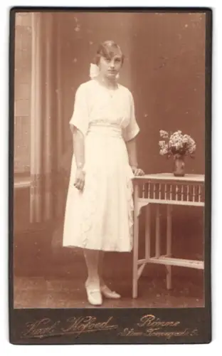Fotografie Karl Kofoed, Rønne, Store Torvegade 5, Junge Frau in weissem Kleid neben Tisch mit Blumen