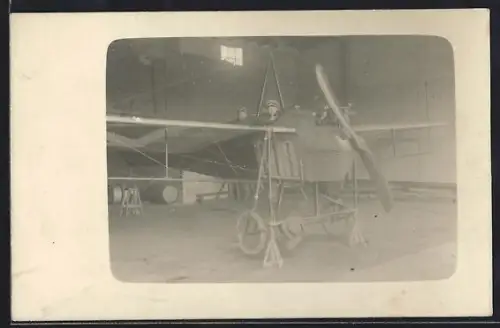Foto-AK Eindecker-Flugzeug im Flugzeugschuppen, Kind mit Gewehr auf dem Pilotensitz