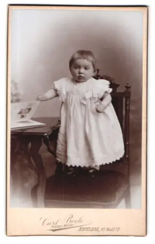 Fotografie Carl Bock, Anklam, Kl. Wall 12, Kind in weissem Kleid an Tisch