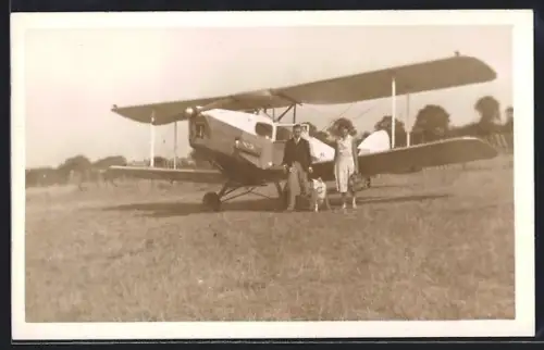 AK Doppeldecker-Flugzeug auf Flugfeld, Frau und Mann mit ihrem Hund nebem dem Flugzeug