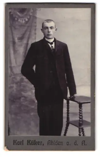 Fotografie Karl Küker, Ahlden a. d. A., Eleganter junger Mann neben Tisch