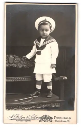 Fotografie A. Dilger & Sohn, Freiburg i/B, Rheinstrasse 30, Kind in Matrosenanzug auf Stuhl