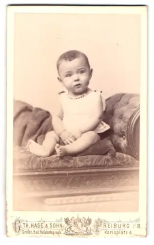 Fotografie Th. Hase & Sohn, Freiburg, Karlsplatz 4, sitzendes Kleinkind auf gepolstertem Stuhl