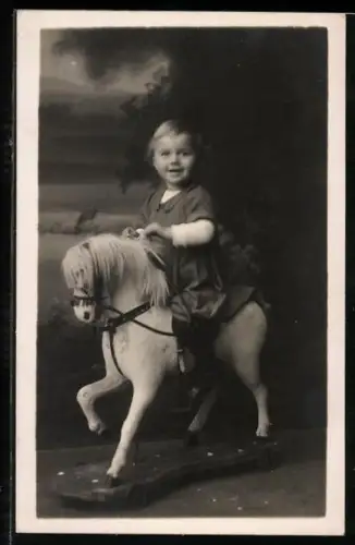 AK Kind sitzt lächelnd auf einem Schaukelpferd