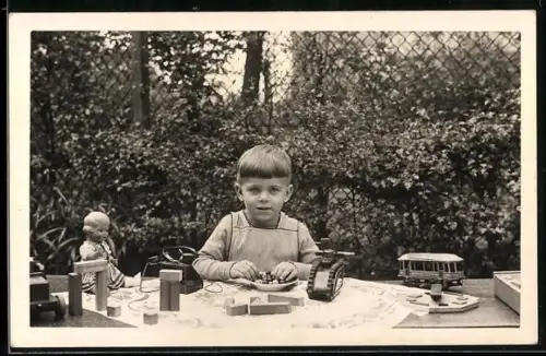 Foto-AK Kind in einem Garten mit Blechspielzeug, Puppe, Bauklötzen und Strassenbahnspielzeug