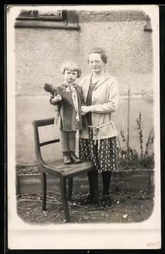 Foto-AK Kind mit Teddybären steht neben seiner Mutter auf einem Stuhl