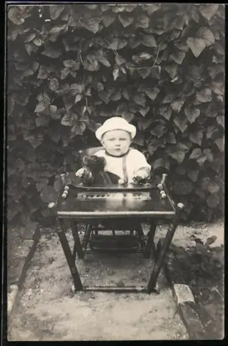 Foto-AK Kleinkind sitzt mit einem Teddy an einem Tisch im Garten