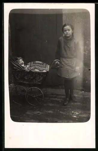 AK Junges Kind mit einem Kinderwagen, in dem eine Puppe liegt